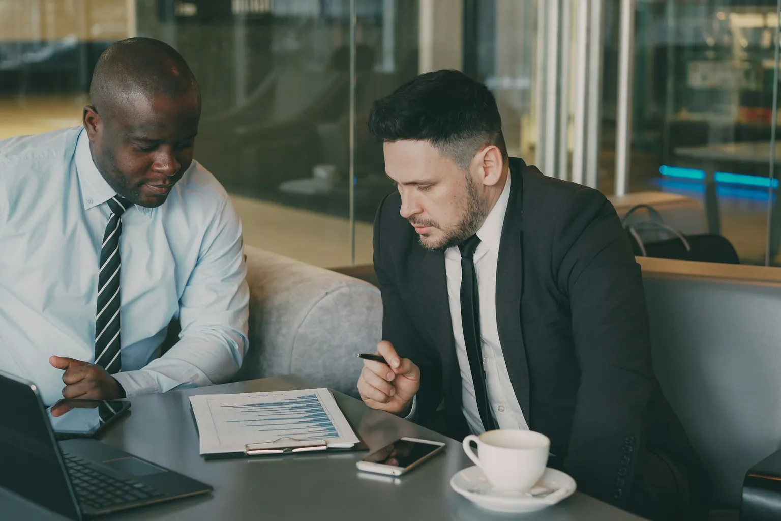 Two colleagues at a table reviewing a printed results chart beside a laptop
